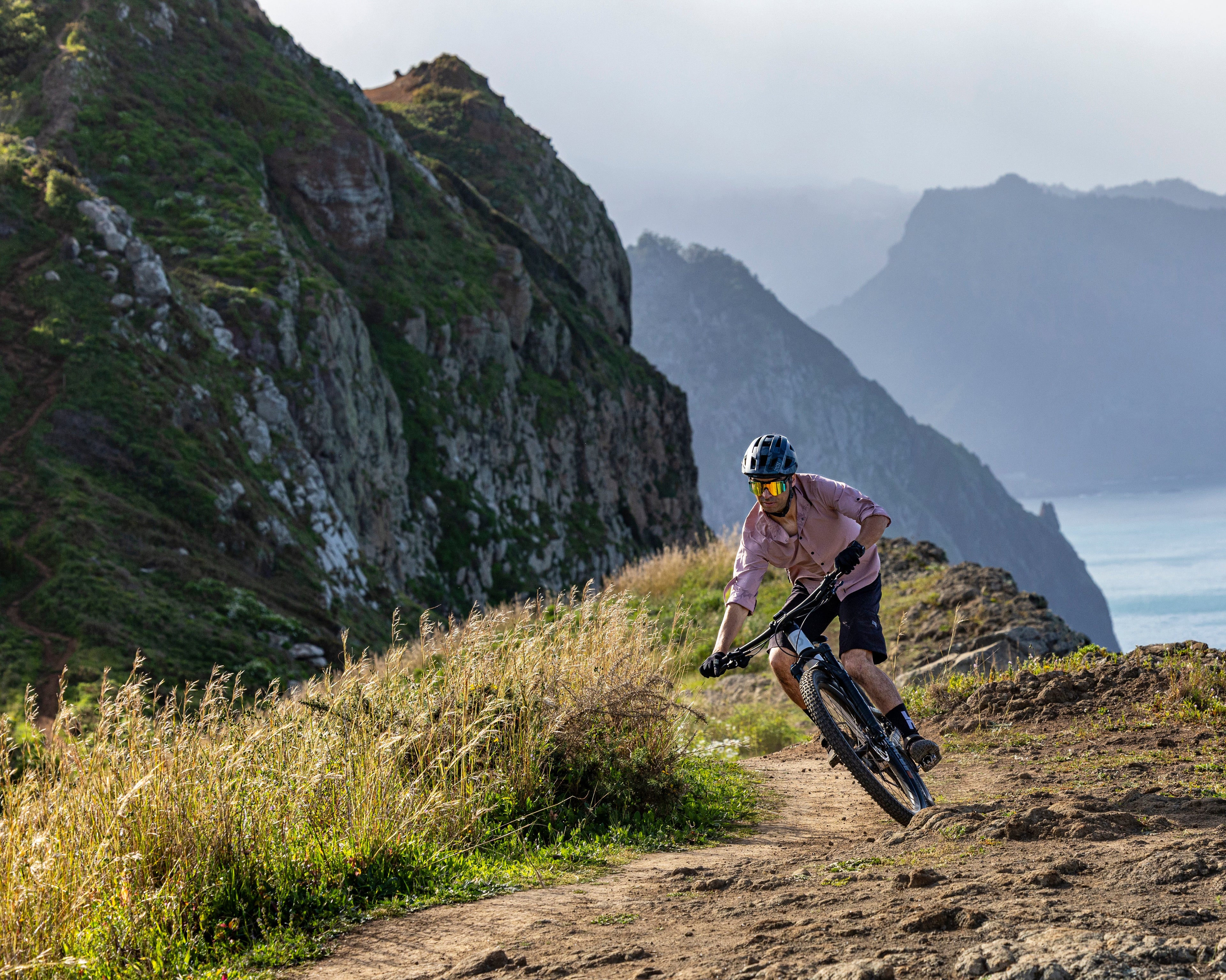 Person mountain biking on a trail with scenic mountains and water in the background
